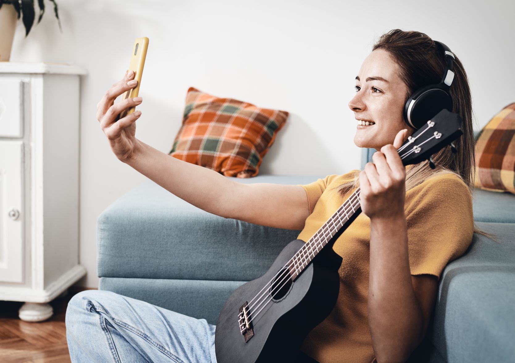 Young woman playing guitar, taking a selfie on her phone