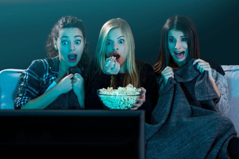 Group of female friends watching scary movie, eating popcorn