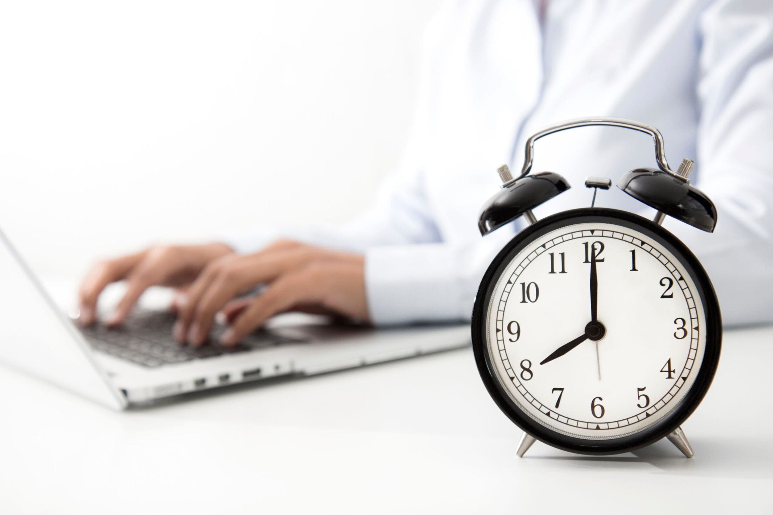 Working hours, clock next to apprentice working on laptop